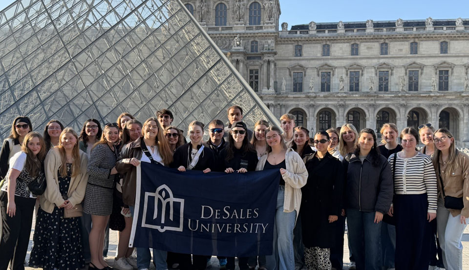 group of students holding a DeSales flag in front of the Louve in Paris, France
