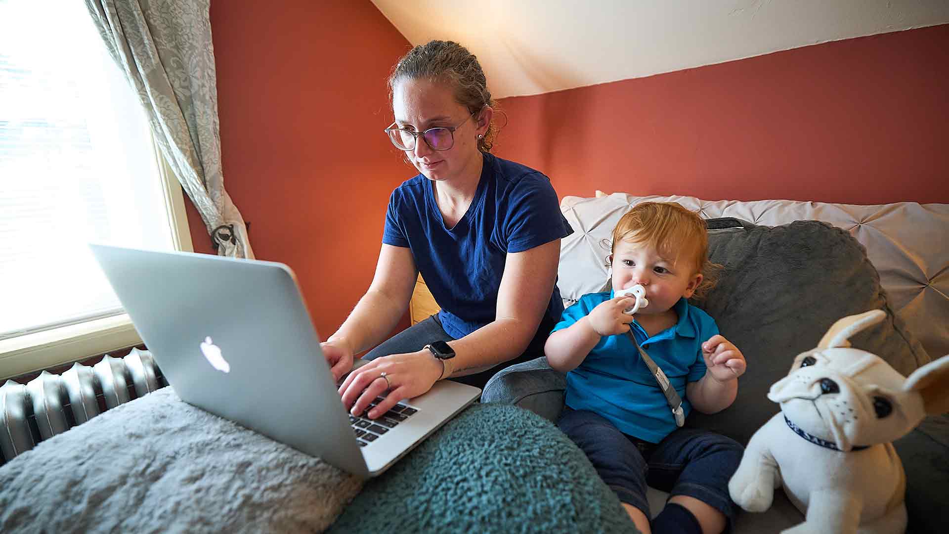 female student doing classwork on laptop at home with child