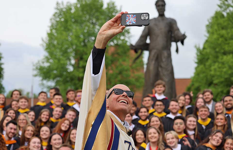 Father Jim taking a selfie with students in front of Jesus statue on campus
