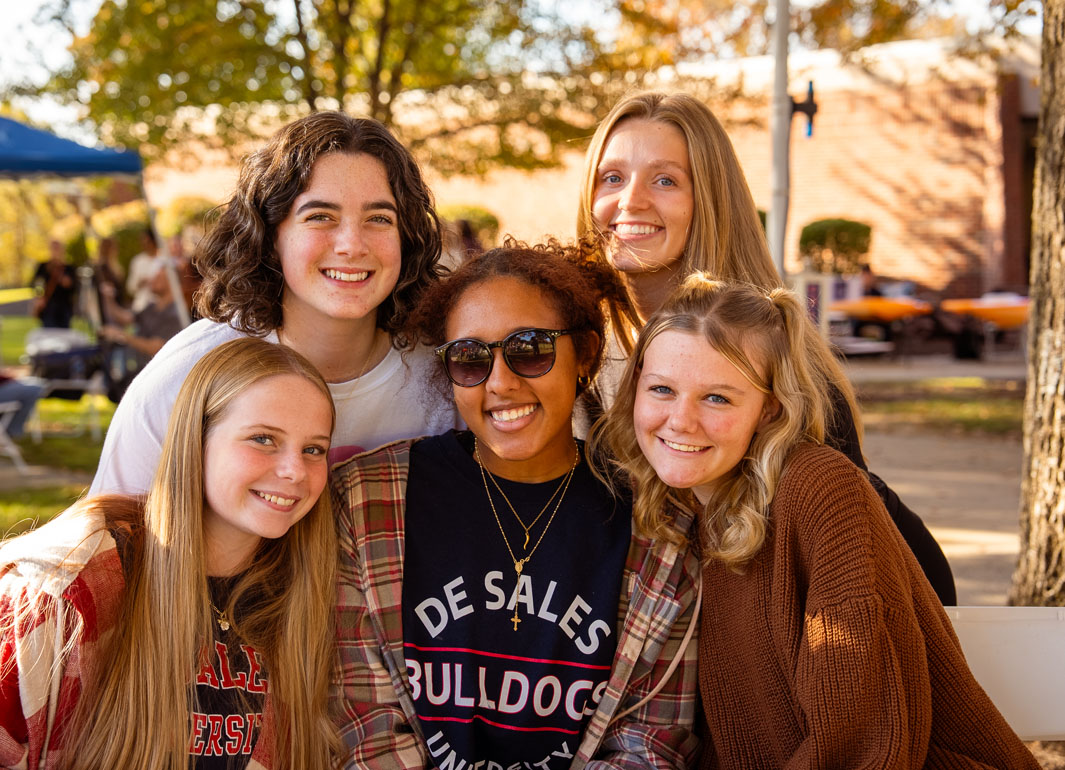 five students smiling at the camera and enjoying a day outside on campus
