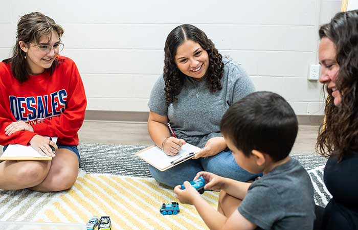 female students sitting on the floor assessing the speech patterns of a young boy