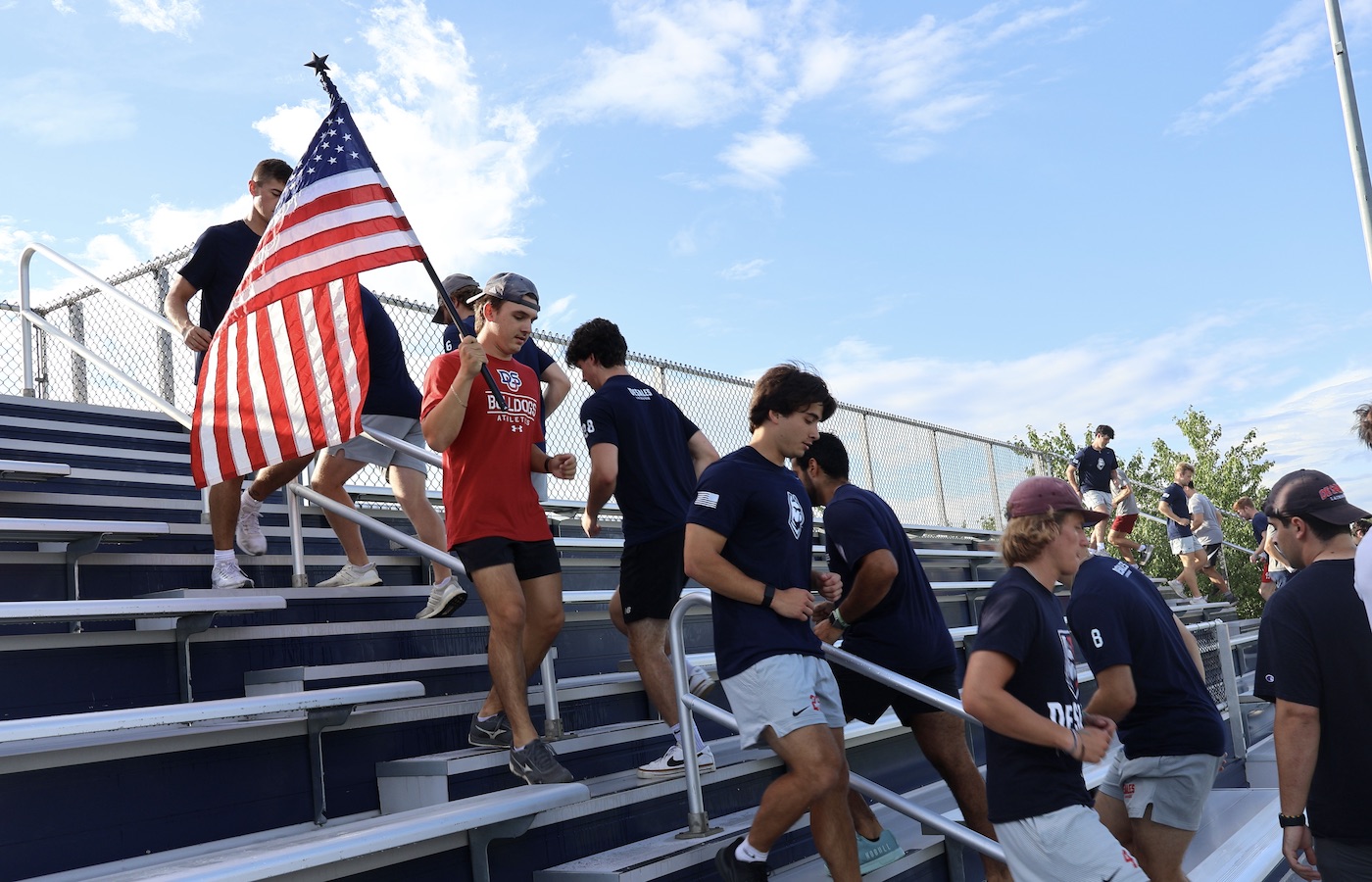 Lacrosse team climbing up bleacher stairs with an American flag